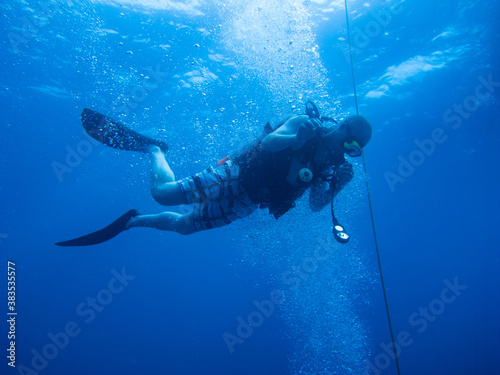 Male scuba diver in blue ocean with bubbles rising around open water