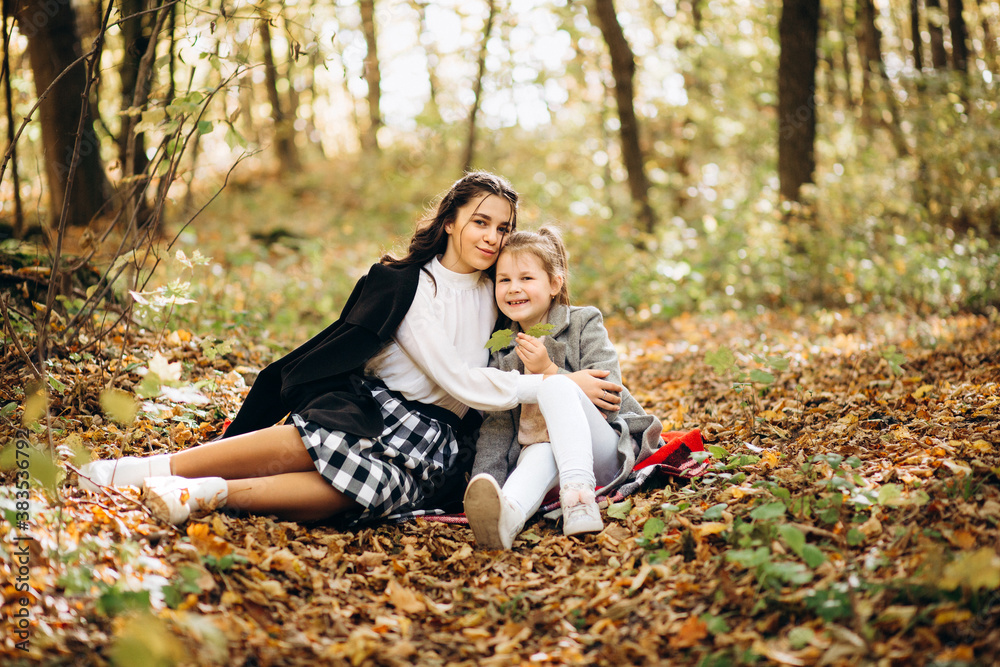 Autumn weekend in the forest mood. The sisters sit on a yellow leaf in the sunny forest and have fun Autumn weekend in the forest mood. The sisters sit on a yellow leaf in the sunny forest and have fun