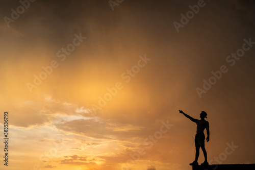 Man standing on the edge rising hands on dramatic orange sunset background. Concept of desire and achievement 
