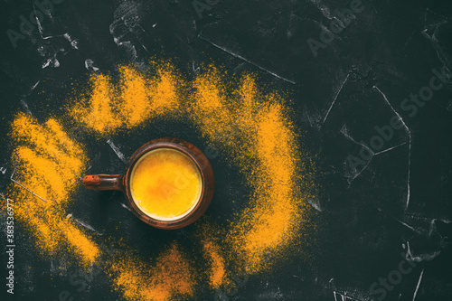 Golden milk with turmeric powder on a black stone background. Top view, copy space. Remedy for flu and colds. Healthy food concept.