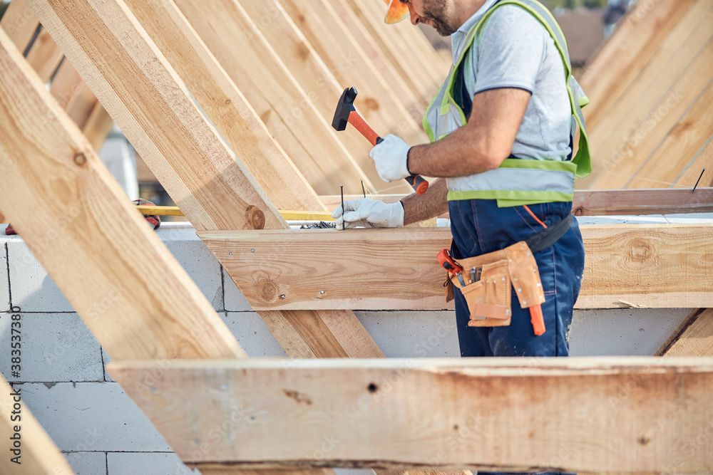 Concentrated man putting a nail into a wooden frame