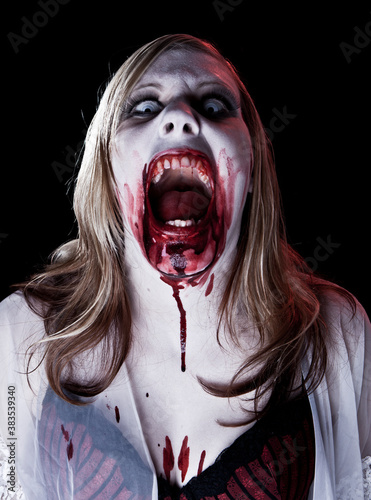 Dark studio photo of a female zombie or vampire with blonde hair on black background.
