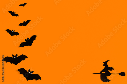 Silhouettes of a flock of bats and a witch flying on a broom made of black paper on an orange background. Halloween greeting template with copy space. Flat lay for your design. ready-made template
