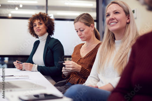 Businesswoman Looking At Mobile Phone During Presentation By Colleague In Modern Office photo