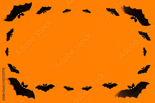 silhouettes of black paper bats on an orange background forming a frame, a flock of black bats on an orange background, Halloween concept, copy space. Flat lay for your design