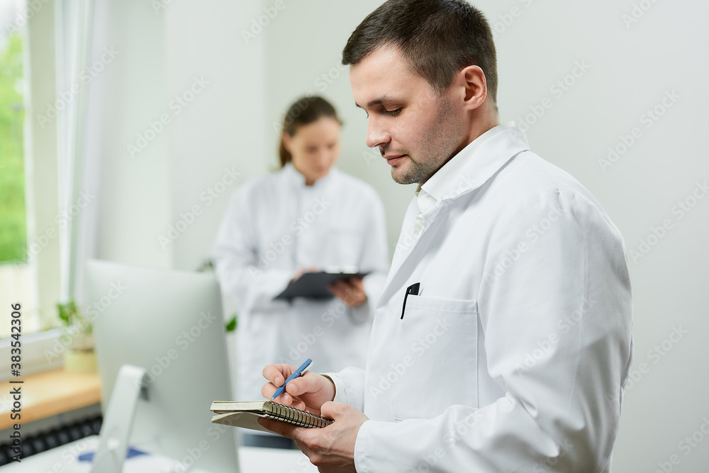 A caucasian doctor with a notebook and a pen records the patient’s medical history in a hospital. A female therapist is doing notes in a clipboard near an all in one computer in a clinic. A caucasian doctor with a notebook and a pen records the patient’s medical history in a hospital. A female therapist is doing notes in a clipboard near an all in one computer in a clinic.