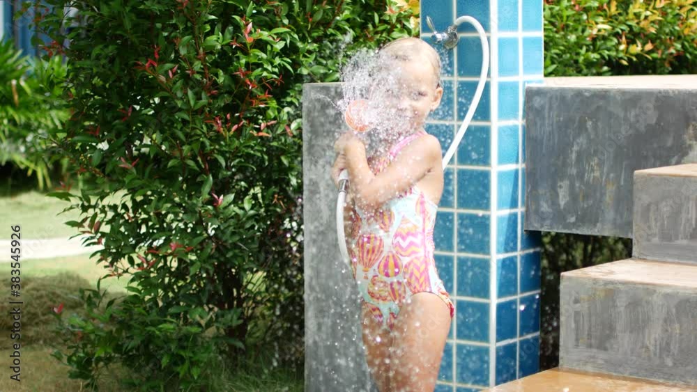 6 year old girl in a swimsuit takes a shower after swimming in the pool