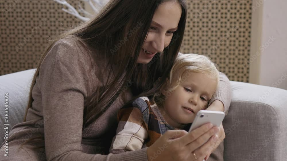 Mother and daughter make phone calls, communicate via video, use a smartphone on Christmas morning. Young mom with her little daughter accept greetings from relatives by the Christmas tree. Mother and daughter make phone calls, communicate via video, use a smartphone on Christmas morning. Young mom with her little daughter accept greetings from relatives by the Christmas tree.