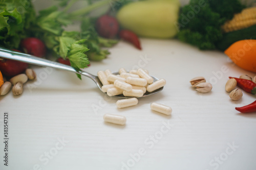 capsules of probiotics and vitamin D3 on the surface of spoon near fresh vegetables and nuts
