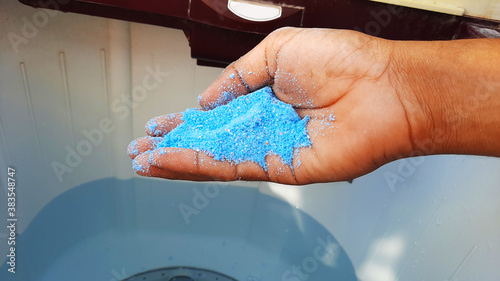 Blue detergent powder in hands and adding it in water in washing machine