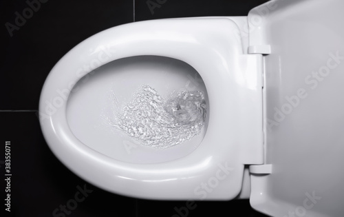 The white flush toilet bowl that the water is draining. concept of flushing away something.