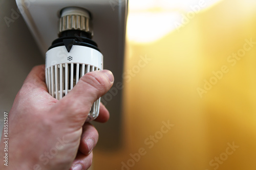 Hand of man adjusting radiator thermostat valve to snow flake frost icon, symbol for saving money at heating costs or low temperature