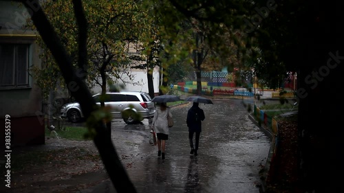 Wallpaper Mural A man and a woman walk down the street with umbrellas on a rainy autumn day. In rainy weather, two people walk under umbrellas, through puddles and on a wet sidewalk. Depressive autumn weather. Torontodigital.ca