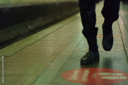 Defocused image. Selective focus. Modern social photography. Sign in Russian "Keep social distancing, 1.5 - 2 meters". Coronavirus pandemic. Human feet at the subway platform. Low angle view