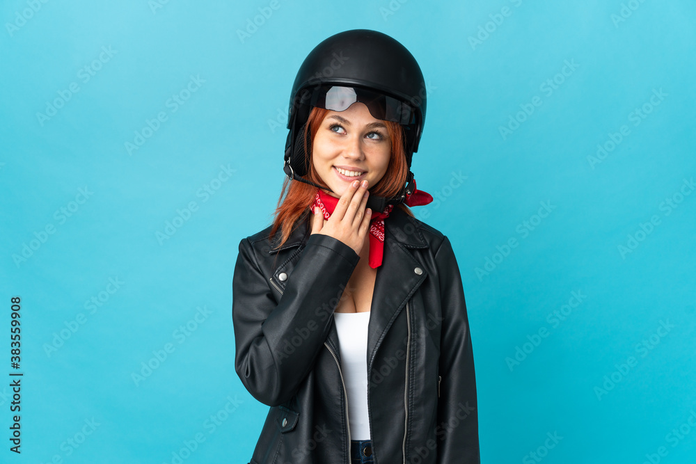 Teenager biker girl isolated on blue background looking up while smiling Teenager biker girl isolated on blue background looking up while smiling