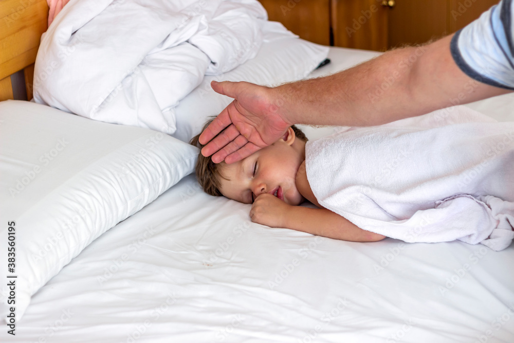 Shot of father is checking temperature on his sick boy at home in bedroom.Sick little boy lying in bed.Father is touching forehead to his sick son checking fever.Worried dad measuring son temperature. Shot of father is checking temperature on his sick boy at home in bedroom.Sick little boy lying in bed.Father is touching forehead to his sick son checking fever.Worried dad measuring son temperature.