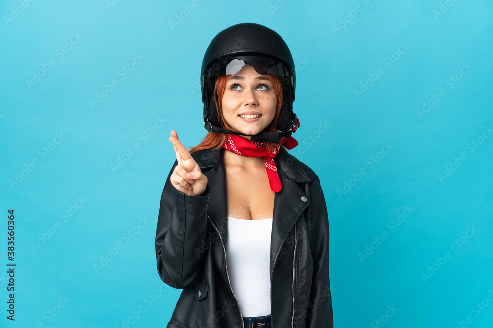 Teenager biker girl isolated on blue background with fingers crossing and wishing the best Teenager biker girl isolated on blue background with fingers crossing and wishing the best