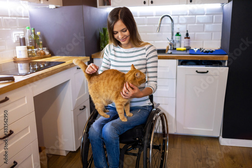 Disabled young woman in kitchen with cat on her lap
