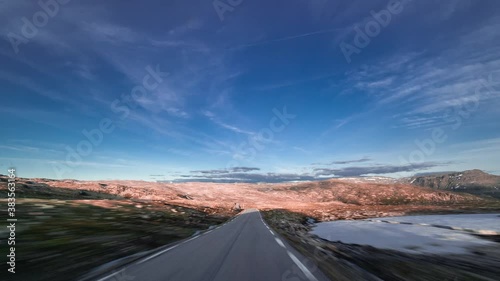 A drive on Aurlandsfjellet road in Norway. Narrow twolane freeway leading through the mountaineous plateau. The harsh tundra landscape is the color of rust. Feathery clouds flow on the bright blue sky photo