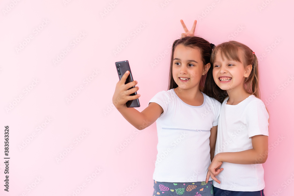 two little girls with a smartphone on a pink background