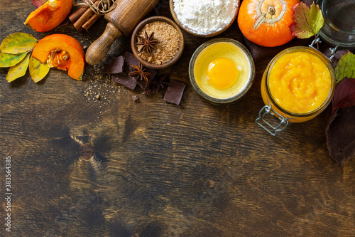 Seasonal food background - ingredients for autumn baking (pumpkin puree, eggs, flour, chocolate, sugar and spices) on a wooden table. Copy space.