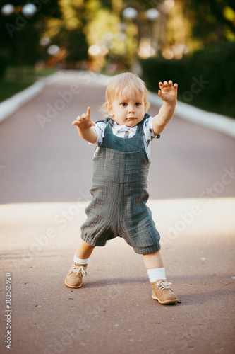 a happy child dressed in a muslin jumpsuit is resting on the green grass.