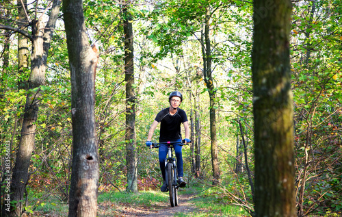 caucasian man in a helmet and sport gloves rides on the bike in the green forest between trees