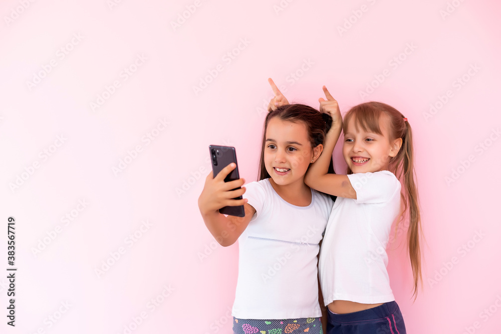 Two little girls playing with smartphones on a pink background Two little girls playing with smartphones on a pink background