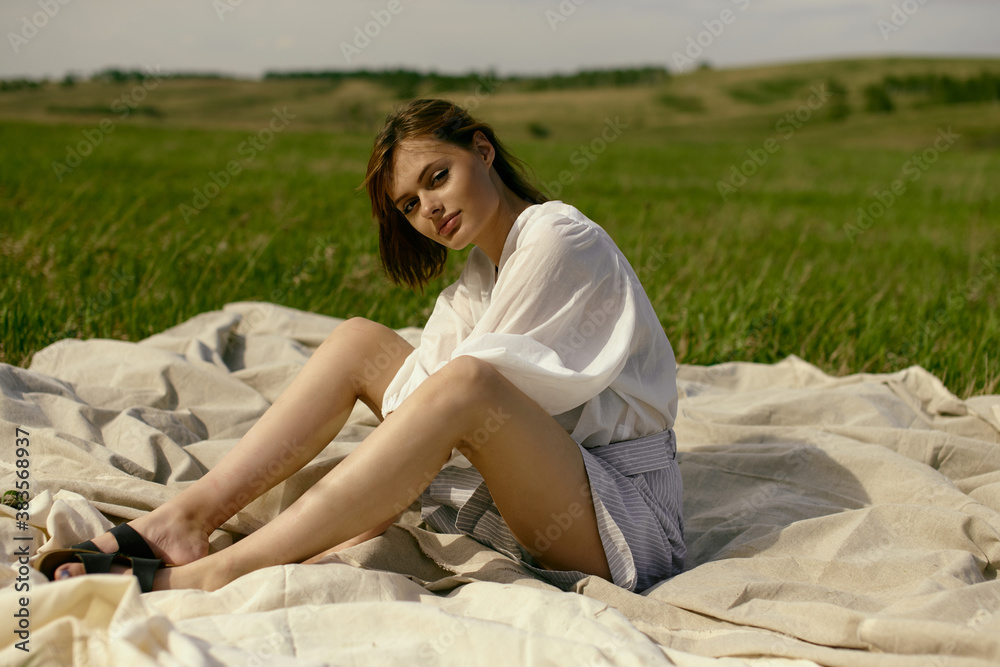 Nice picnic on the grass. Young beautiful woman in the middle of green field. Summer landscape, good weather. Windy day with sun and clouds. Cotton white suit eco style. Nice picnic on the grass. Young beautiful woman in the middle of green field. Summer landscape, good weather. Windy day with sun and clouds. Cotton white suit eco style.