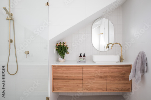 Photographie Brushed brass tap mixer on timber vanity with white basin bowl against white til