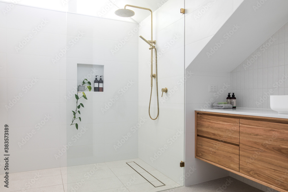 Brushed brass tap mixer on timber vanity with white basin bowl against white tiled wall in a new modern elegant bathroom lit by natural light from a nearby window modern interior house renovation new  - obrazy, fototapety, plakaty 