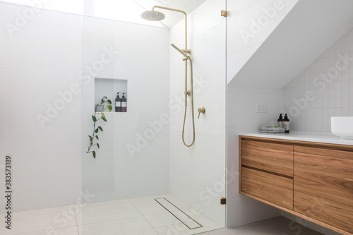Brushed brass tap mixer on timber vanity with white basin bowl against white tiled wall in a new modern elegant bathroom lit by natural light from a nearby window modern interior house renovation new  photo