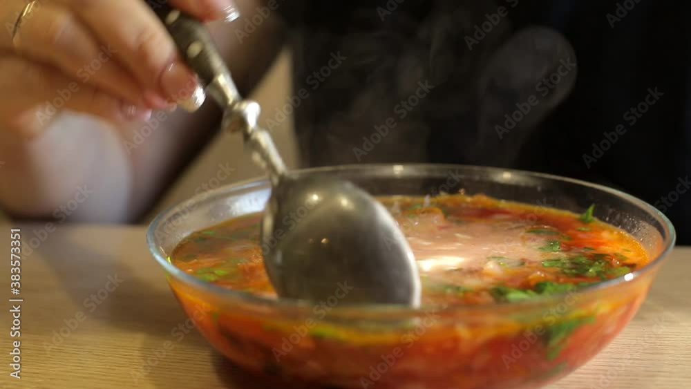 a woman eats cabbage soup with vegetables and meat in a transparent plate, adds fresh herbs and sour cream , home-made food a woman eats cabbage soup with vegetables and meat in a transparent plate, adds fresh herbs and sour cream , home-made food