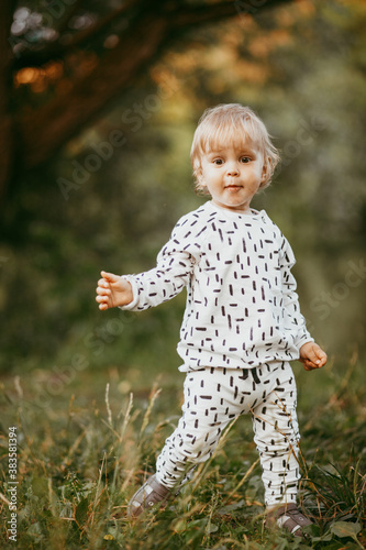 boy walking in a beautiful white suit against the background of nature  baby about one year old learning and playing outdoors.