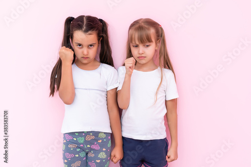 Image of two angry teenage girls with braids in casual clothes standing isolated over pink background