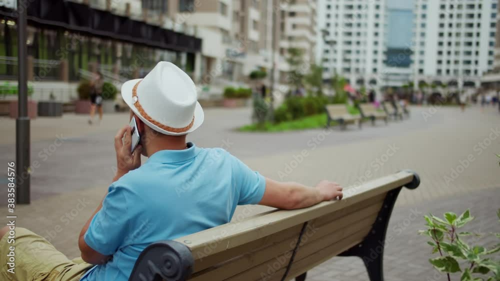 Young man in a hat talking on the phone while sitting on a bench, camera movement, copy space Young man in a hat talking on the phone while sitting on a bench, camera movement, copy space