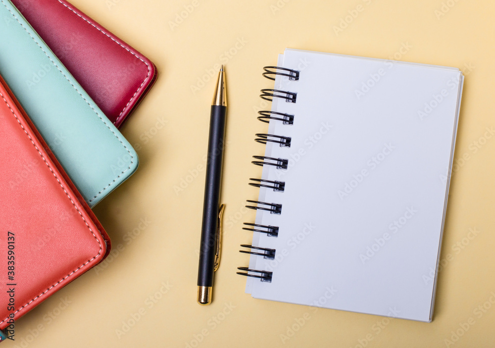 Multi-colored diaries lie on a beige background near a blank notebook and a pen. Flat lay. Copy space Multi-colored diaries lie on a beige background near a blank notebook and a pen. Flat lay. Copy space
