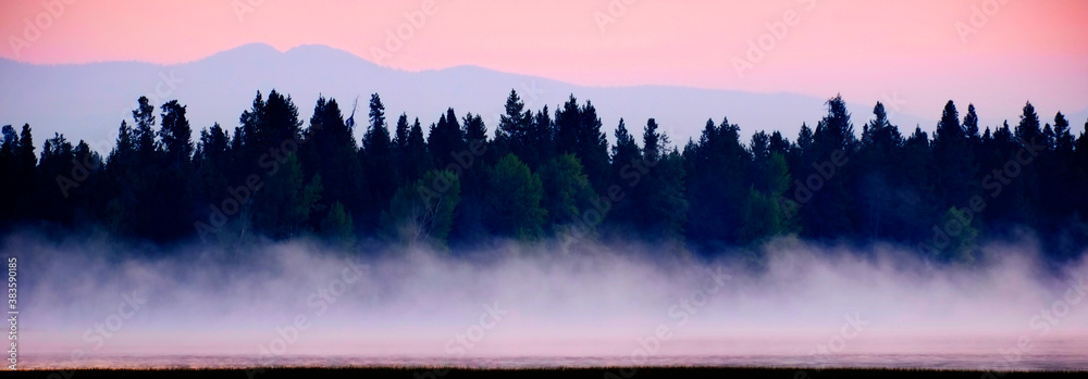 Sunrise Sunset on Lake with Mist Rising from Water Pine Trees and Mountains in Background