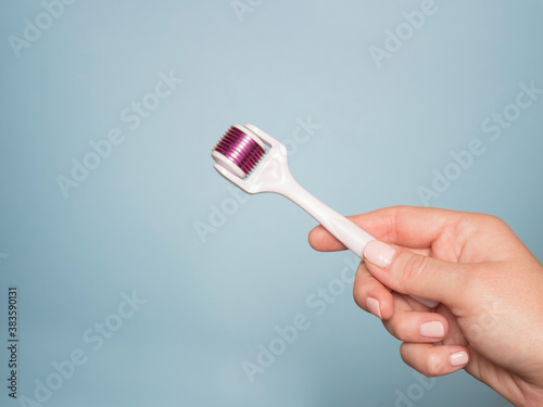 Hand and mesoroller in hand on a blue background. Scalp and skin care, healthy hair. photo