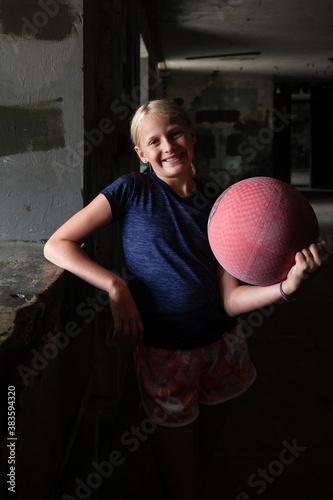 Blond girl holding a red kickball in a dark room