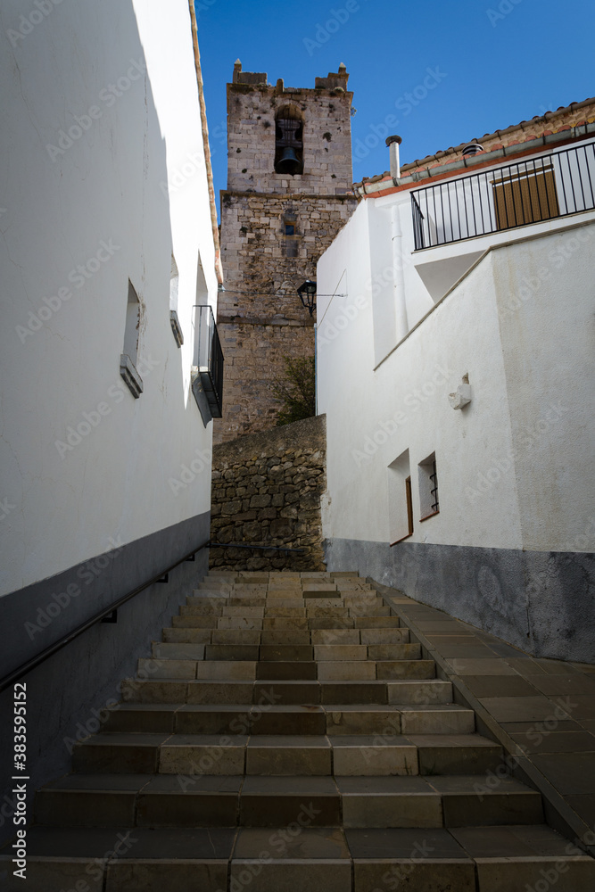 Narrow street of the medieval town of Ares del Maestre with the Church of the Assumption of Our Lady in the background on a blue day, Castellon, Spain