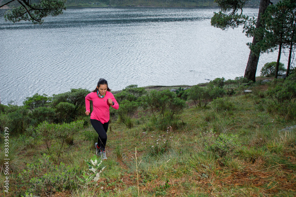 Atleta corriendo en el bosque subiendo una montaña que esta cerca de un lago Atleta corriendo en el bosque subiendo una montaña que esta cerca de un lago