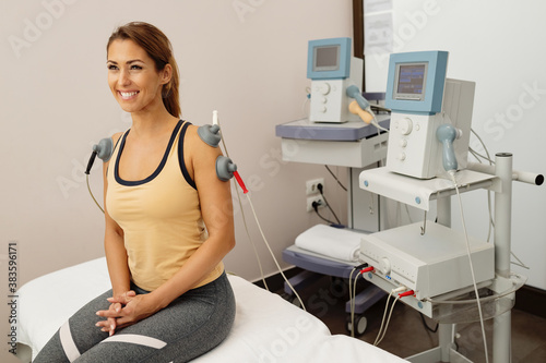 Happy athletic woman receiving electrotherapy treatment for injured shoulders at the clinic. photo