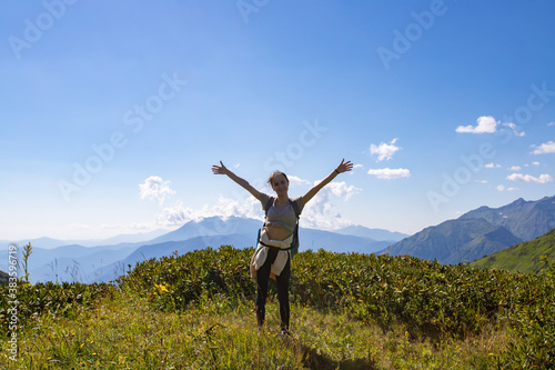 A girl stands on top of a mountain hands up, freedom, happiness concept