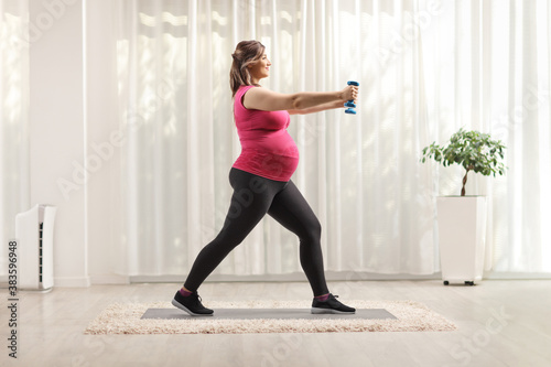 Full length profile shot of a pregnant woman exercising with blue dumbbells
