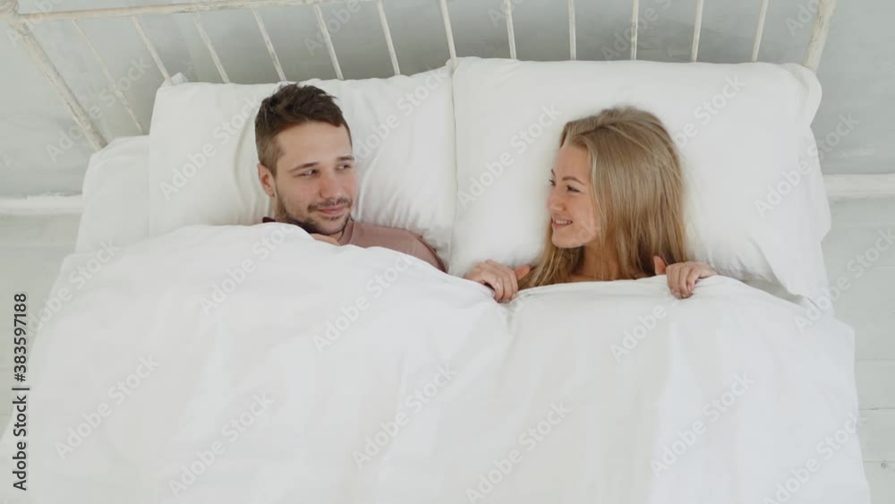Happy young woman and man falls on the white bed in room. Lovers looking to each other Happy young woman and man falls on the white bed in room. Lovers looking to each other