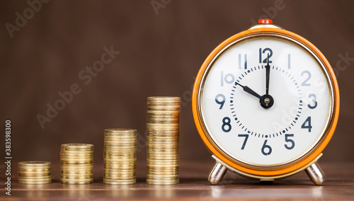 Money savings, growing concept, gold coins with alarm clock on brown background with copy space