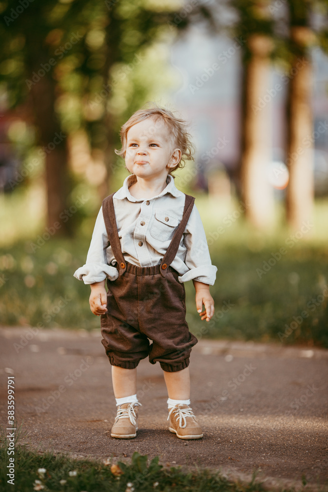 Fototapeta premium A small blond boy dressed in a vintage jumpsuit in a field at sunset