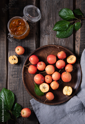 juicy mini apples in a plate with linen towel and a jar of jam on a old wooden background.