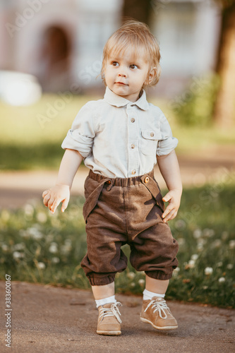 A small blond boy dressed in a vintage jumpsuit in a field at sunset